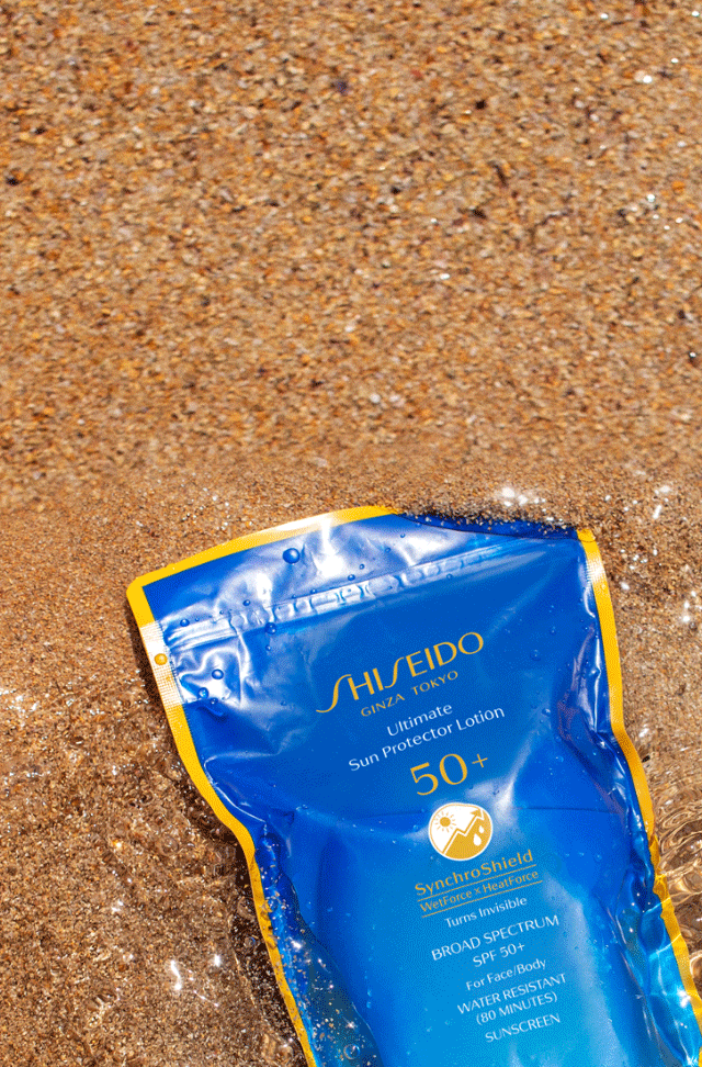 Sandy beach with waves washing over Shiseido Suncare products.